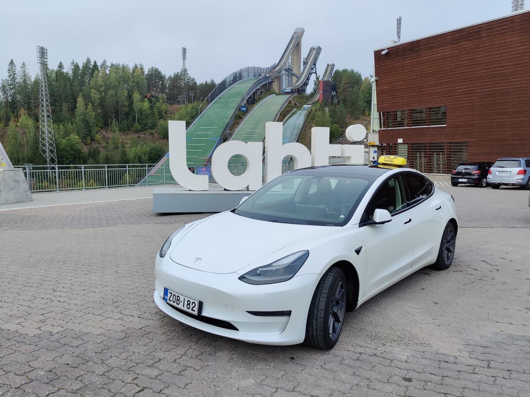 Valkoinen Tesla Model 3 -taksi Lahden hyppyrimäkien edessä