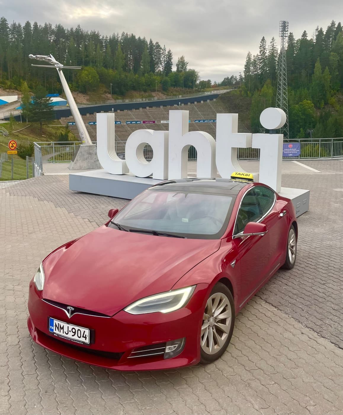 Punainen Tesla Model S -taksi Lahti-kyltin edessä